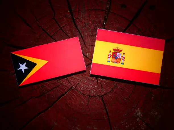 Photo of East Timorese flag with Spanish flag on a tree stump isolated