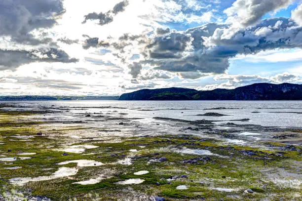 Fjord in Saguenay river closeup of beach shore with shallow water and cloudy sky