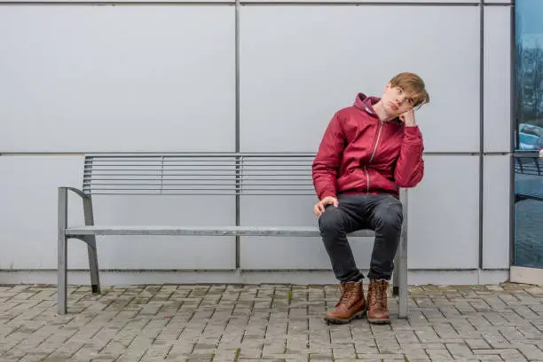 Photo of Bored teenage boy sitting on bench in city