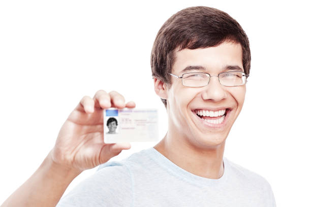 Guy with driving license Close up portrait of young hispanic man wearing glasses and blue t-shirt holding out his driving license and smiling isolated on white background - new drivers concept drivers license photos stock pictures, royalty-free photos & images