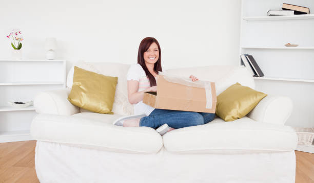 istock Beautiful redhaired female opening a carboard box while sitting on a sofa 827102206