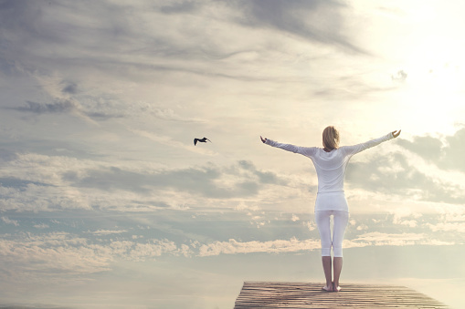 woman with open arms meditating in front of a spectacular sky