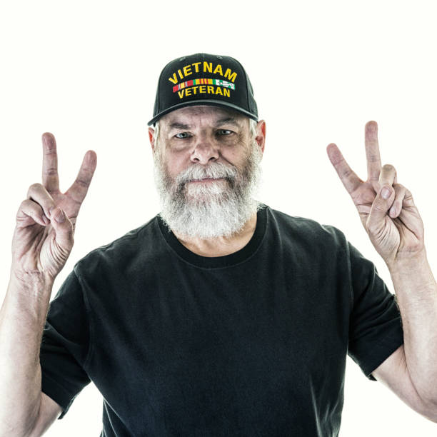 Senior old bearded man showing victory sign, hoping for success and win, doing peace gesture and smiling with kind optimistic expression. Orange studio background. Elderly grandfather pensioner