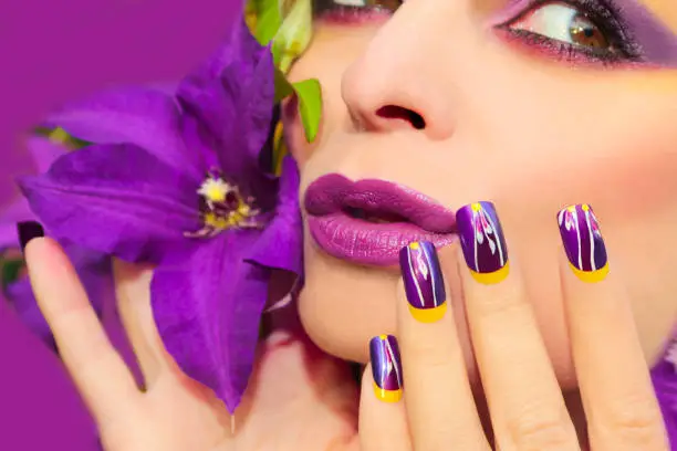 Lilac summer makeup and manicure with a design on the nails on the woman with the clematis closeup.Nail art.