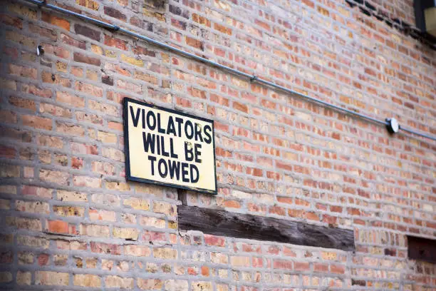Violaters will be towed sign on a brick wall.
