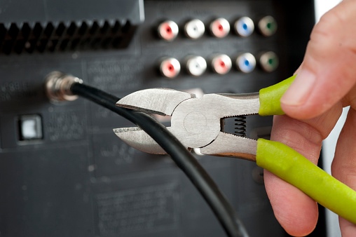 Hand useing wirecutters and cutting a television cable attached to a television set. Wirecutters cut the cable wire.