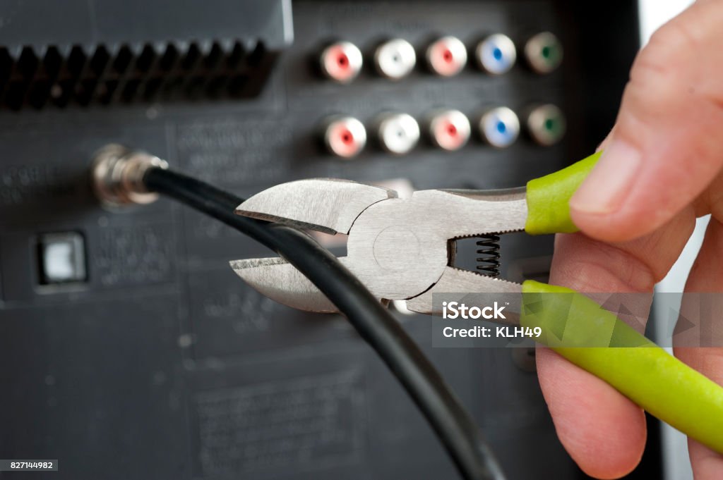 Cut the cable TV cord with hand and wire cutters Hand useing wirecutters and cutting a television cable attached to a television set. Wirecutters cut the cable wire. Cable Stock Photo
