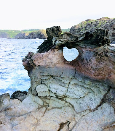 Heart shape geological formation naturally occurring in lava rock wall at Nakalele in Hawaii, USA, with ocean and Maui Mountains in the background landscape with splashing waves