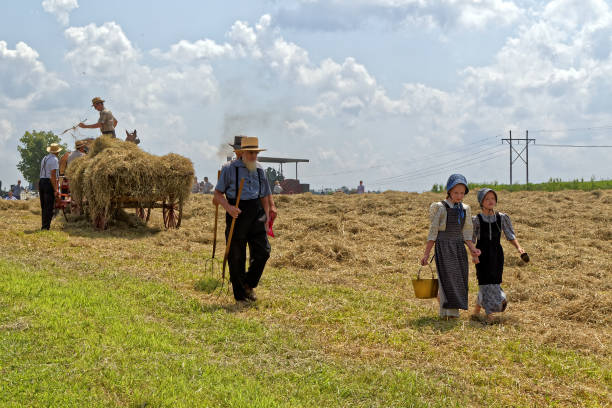 Girls Carry Water for the Hay Crew New Holland, Pennsylvania - August 4, 2017: Two young Mennonite girls with a pail and cup carry water for the hay crew at Big Spring Farm Days. This is an annual event demonstrating traditional threshing and harvesting methods, using restored antique and vintage tools. horse cart photos stock pictures, royalty-free photos & images