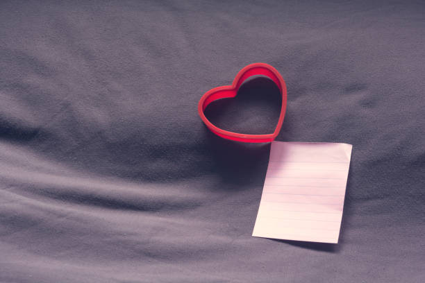 istock Red heart shape and empty note paper on bed. Valentine concept. 827191116
