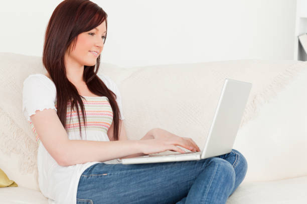 istock Beautiful redhaired woman relaxing with her laptop while sitting on a sofa 827198012