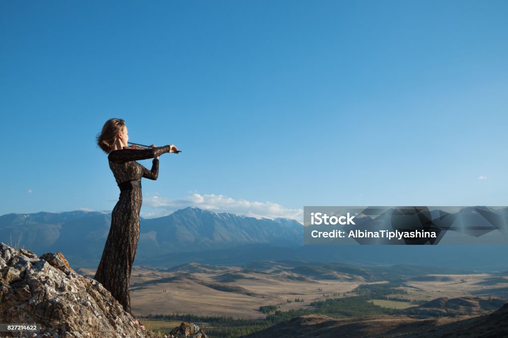 Girl playing violin on nature Girl in concert dress, playing the violin, standing on top of a mountain Adults Only Stock Photo