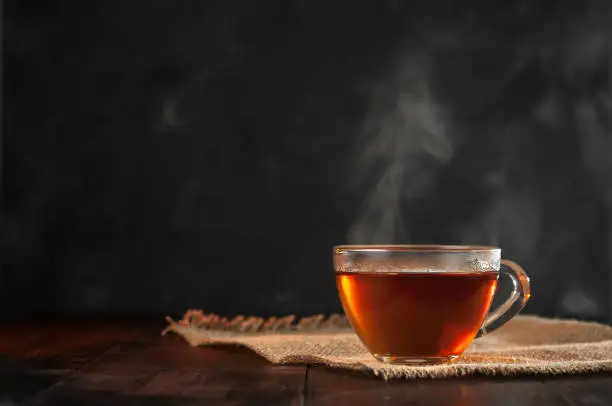 Photo of A Cup of freshly brewed black tea,escaping steam,warm soft light, darker background.