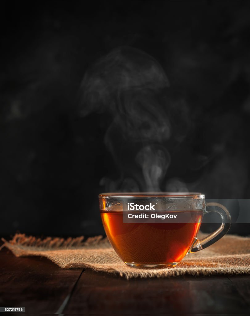 A Cup of freshly brewed black tea,escaping steam,warm soft light, darker background. Drinking Glass Stock Photo