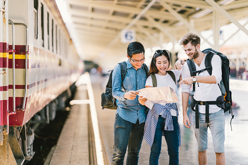 Multiethnic group of friends, backpack travelers, or college students using generic local map navigation together at train station platform. Asia tourism activity or railroad trip travelling concept