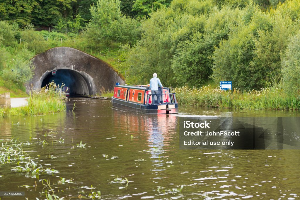 Old fashioned canal barge on the Union Canal, central Scotland Falkirk, Scotland, UK - August 4, 2017: A pedestrian, a cyclist and a person at the helm of a canal barge on the Union Canal near Falkirk in central Scotland. August Stock Photo