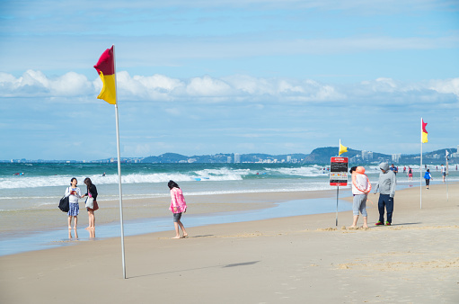 Gold Coast, Australia - July 11, 2017: people on the beach beside red and yellow surf patrol flags at Surfers Paradise.