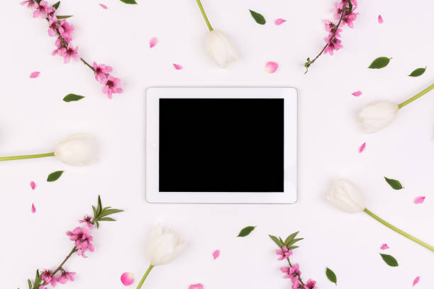 istock tenderness, business, technology concept. top view of white tablet with dark screen surrounded by isolated floral elements such as tender blossoms of tulips, brunches of peach tree and green leaves 827295304