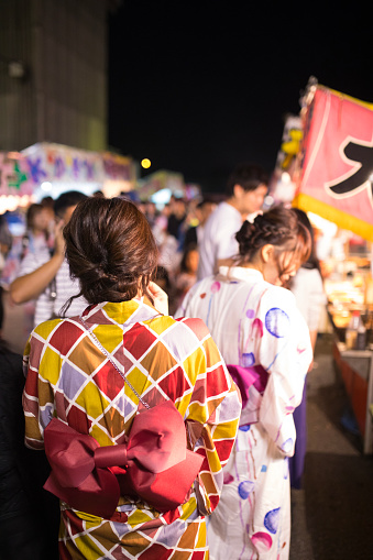 Young women in yukata walking in night market after fireworks show