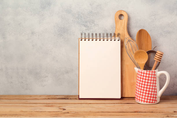 Blank notebook and kitchen utensils on wooden table over rustic background with copy space