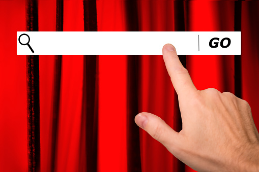 Man searching internet websites for an entertainment event.  Red stage curtains represent concept for theatrical play or movie.