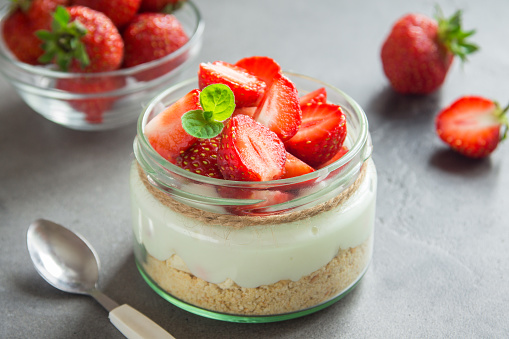 Strawberry cheesecake in glass jar with fresh strawberries and cream cheese  on grey concrete background. Healthy homemade dessert.
