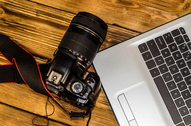 istock Modern DSLR camera and laptop on wooden table. Top view 827362372