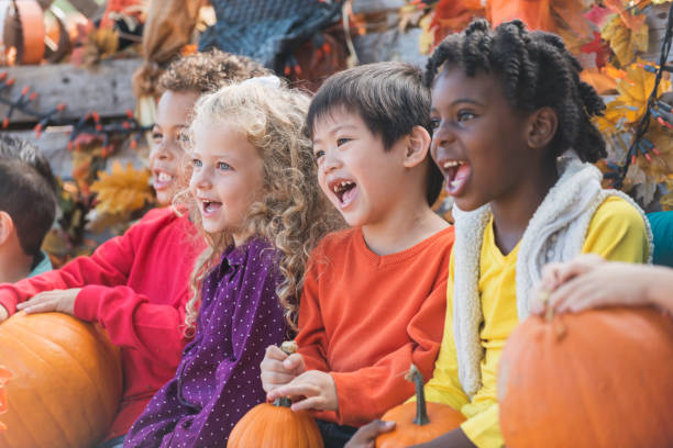 Multi-ethnic children at autumn festival A group of multi-ethnic children at a fall festival, sitting in a row surrounded by pumpkins and autumn colors and decorations, laughing and singing. agricultural fair photos stock pictures, royalty-free photos & images