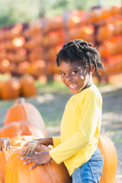 afrikanisch-amerikanischen mädchen in einem kürbisfeld - pumpkin child little girls pumpkin patch stock-fotos und bilder