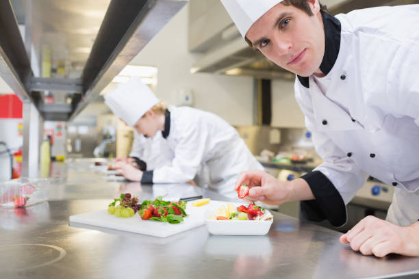 istock Man chef putting a strawberry in fruit salad 827366542