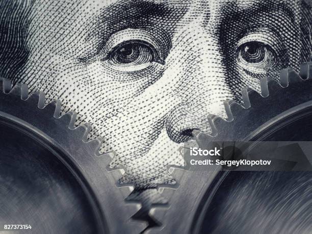 Two Gears Rotate On The Background Of Hundred Dollar Bills Stock Photo - Download Image Now