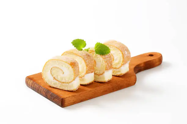 Slices of sponge cake roll with cream filling on cutting board