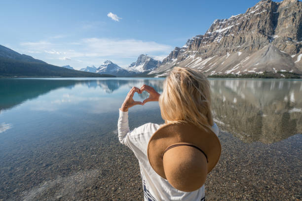 istock Young woman making heart shape finger frame on mountain lake 827394248