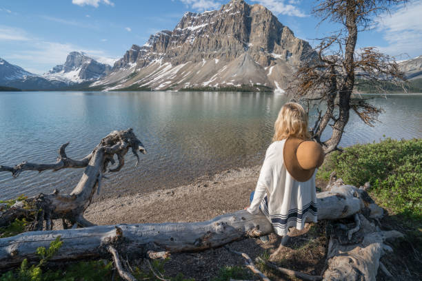istock Young woman sitting on tree trunk at mountain lake 827397450