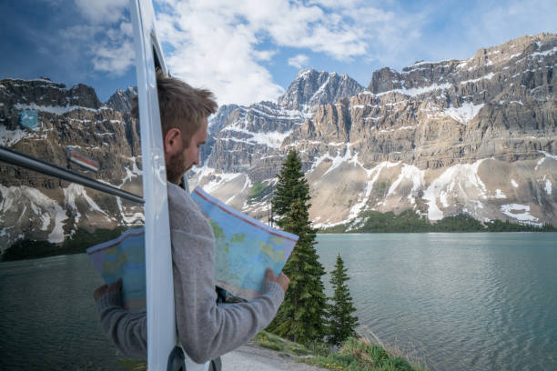 Young man looks at road map near mountain lake Young man in car on mountain road looks at map for directions. Mountain lake landscape in Springtime with snow melting. canada road map stock pictures, royalty-free photos & images