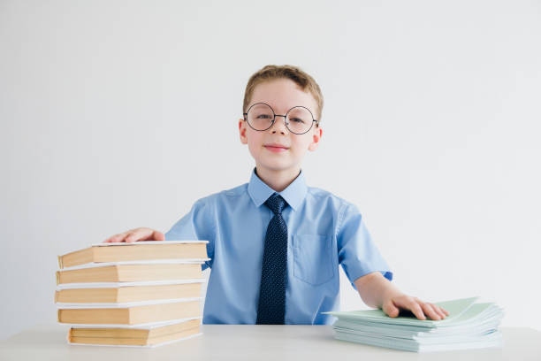 istock Schoolboy in school uniform sitting at a Desk with textbooks and 827412946