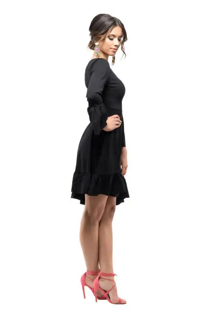 Side view of gorgeous woman in black dress with bun hair looking down. Full body length portrait isolated on white studio background.