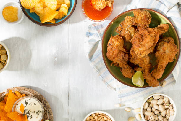 istock rame of fried chicken, sauces, chips, peanuts, pistachios and crackers on a white wooden table 827473546