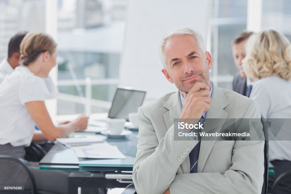 Smiling businessman posing in the boardroom Smiling businessman posing in the boardroom while colleagues are working behind 20-29 Years Stock Photo