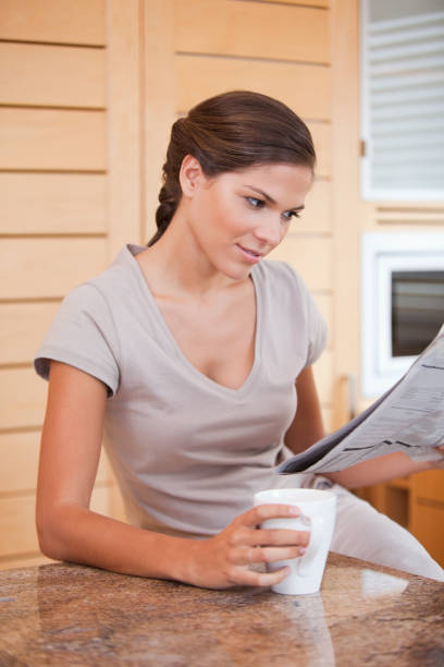 istock Woman reading newspaper while holding cup of coffee 827482530