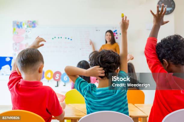 Preschool Kid Raise Arm Up To Answer Teacher Question On Whiteboard In Classroom Kindergarten Education Concept Stock Photo - Download Image Now