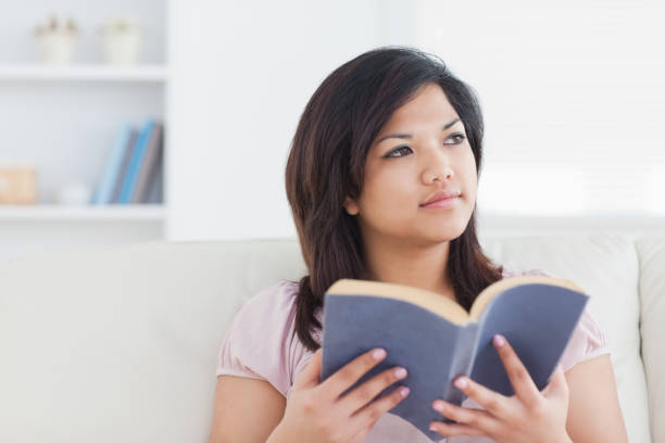 istock Woman sitting on a sofa while holding a book 827491544