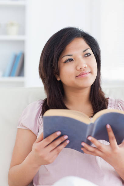 istock Woman sitting on a sofa while she holds a book 827493680