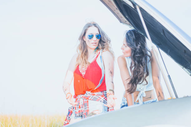 istock Two young woman standing by the broken car, trying to fix engine. 827507142