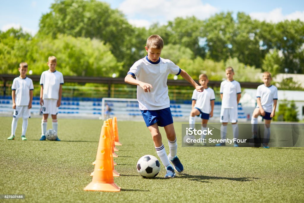 Junior Football Player at Practice Portrait of boy in junior football team  leading ball between cones during  practice in field on sunny day Sport Stock Photo