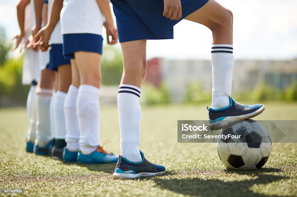 Junior Football Team Ready to Fight Low section portrait of junior football team : legs of boys standing in row with captain stepping on ball in sunlight Soccer Team Stock Photo