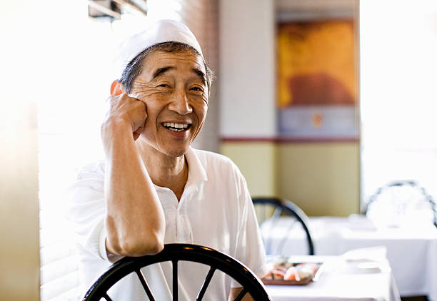 Japanese Chef at restaurant table Smiling Japanese chef seated in restaurant, face resting on hand   japanese chef stock pictures, royalty-free photos & images