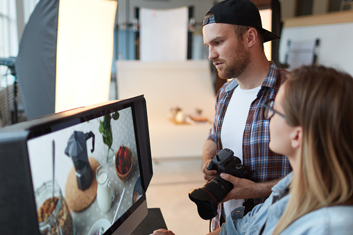 Photographer and designer discussing one of shots on monitor display while choosing best ones