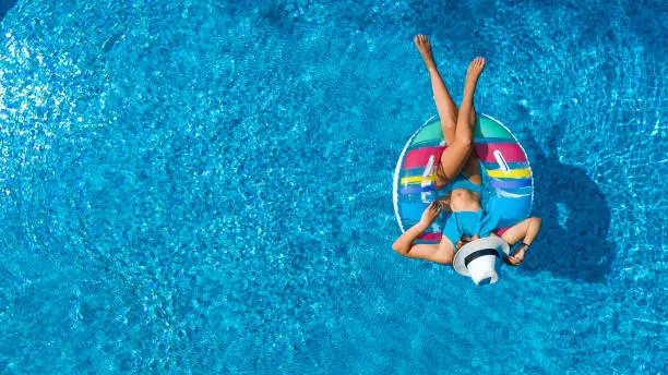 Photo of Aerial view of beautiful girl in swimming pool from above, swim on inflatable ring donut and has fun in water on family vacation