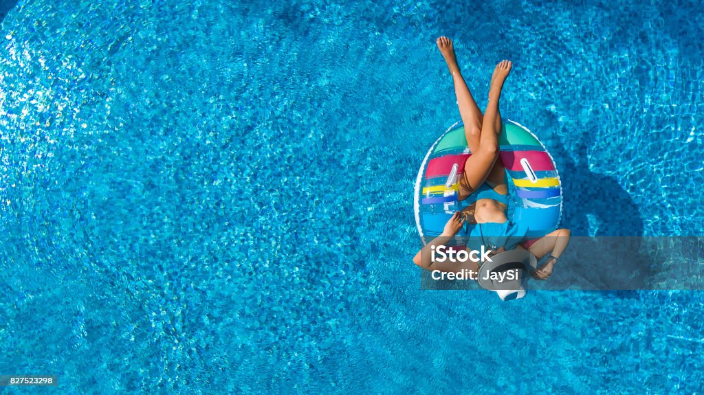 Vista aérea da bela garota na piscina de cima, nadar na rosca do anel inflável e se diverte na água em férias de família - Foto de stock de Piscina royalty-free